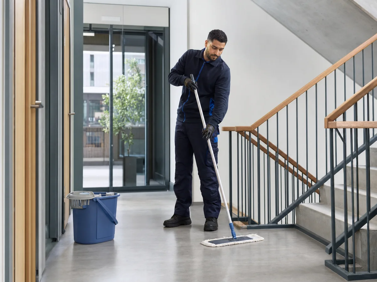 Medewerker dweilt veilig de overloop van een modern trappenhuis